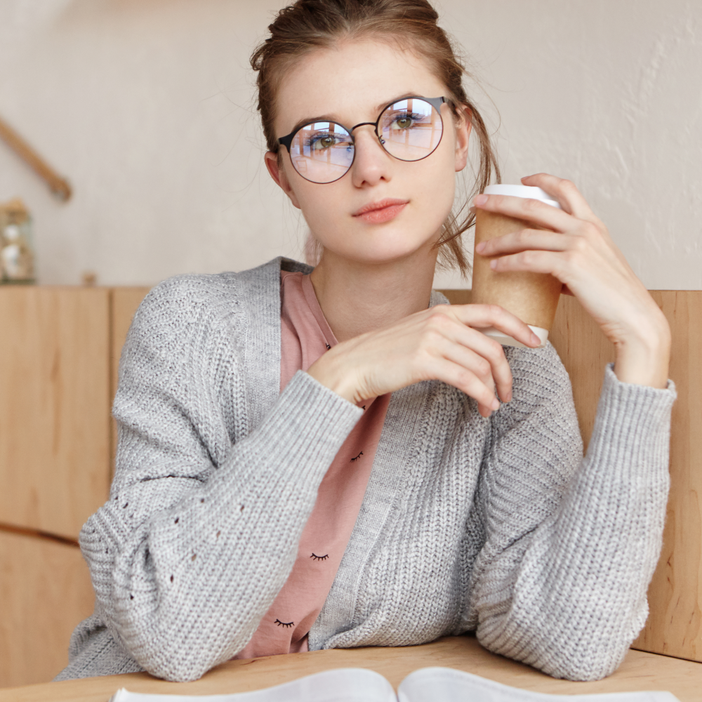 Woman wearing stylish round prescription glasses, sipping coffee in cozy café setting
