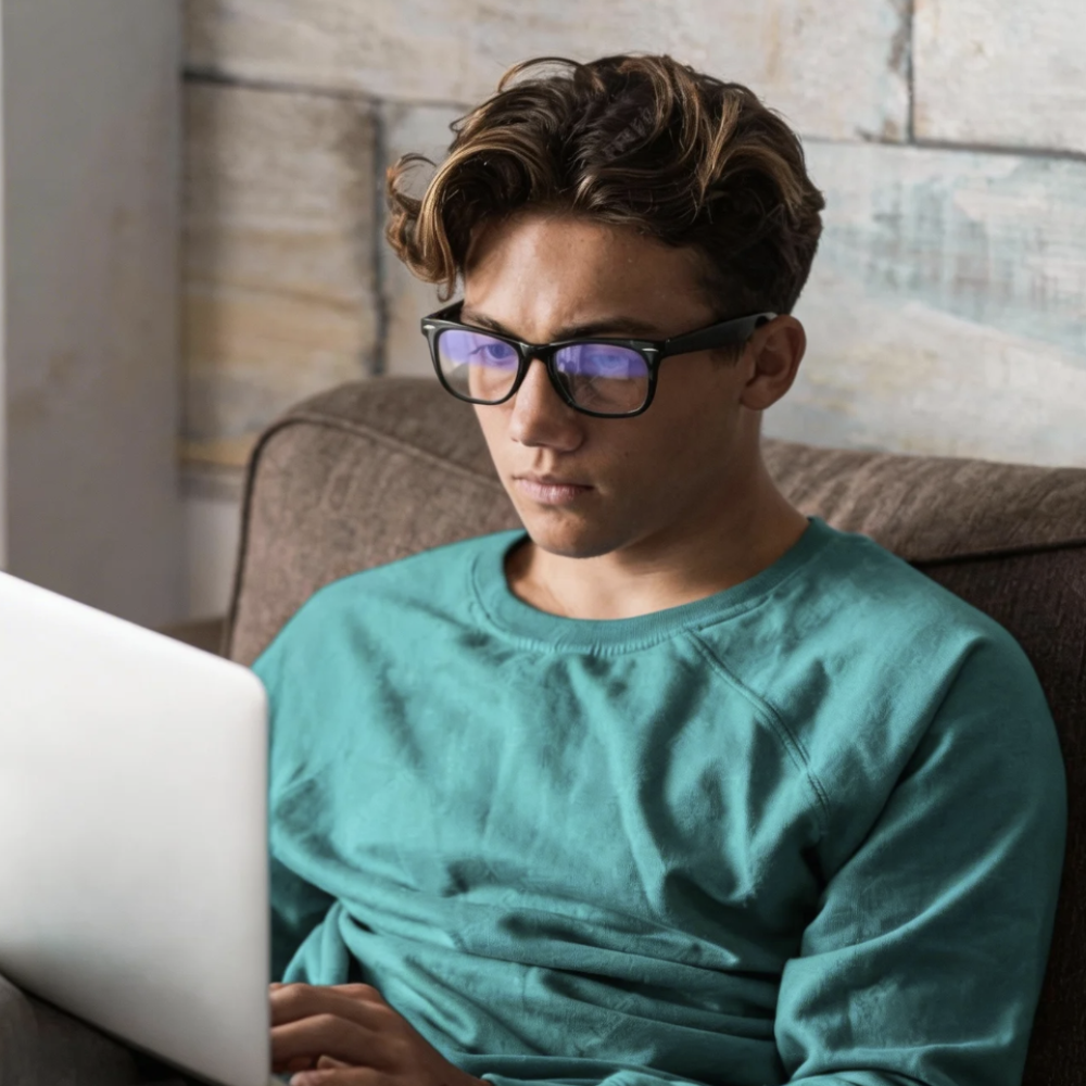 Man wearing stylish black-framed glasses while using laptop, showcasing modern eyewear design