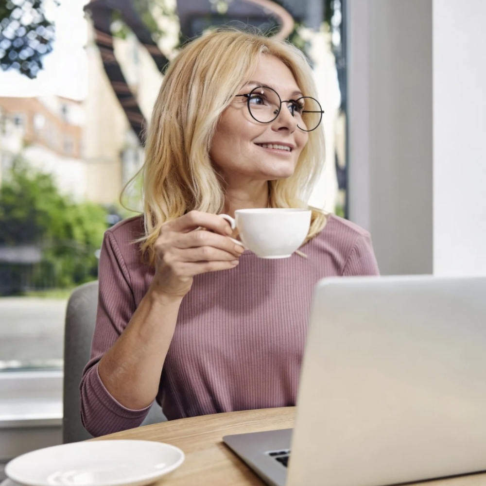 Woman wearing round prescription glasses sipping coffee at laptop, stylish eyewear for everyday elegance