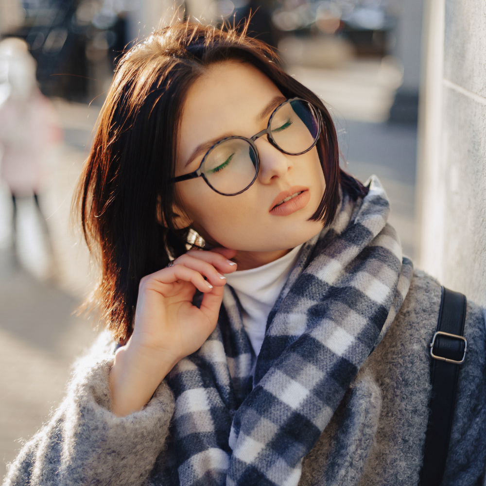 Woman wearing stylish round prescription glasses, cozy scarf, and sweater outdoors